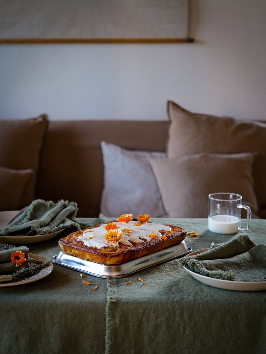 Cake with orange flowers on olive green linen and fringed napkins
