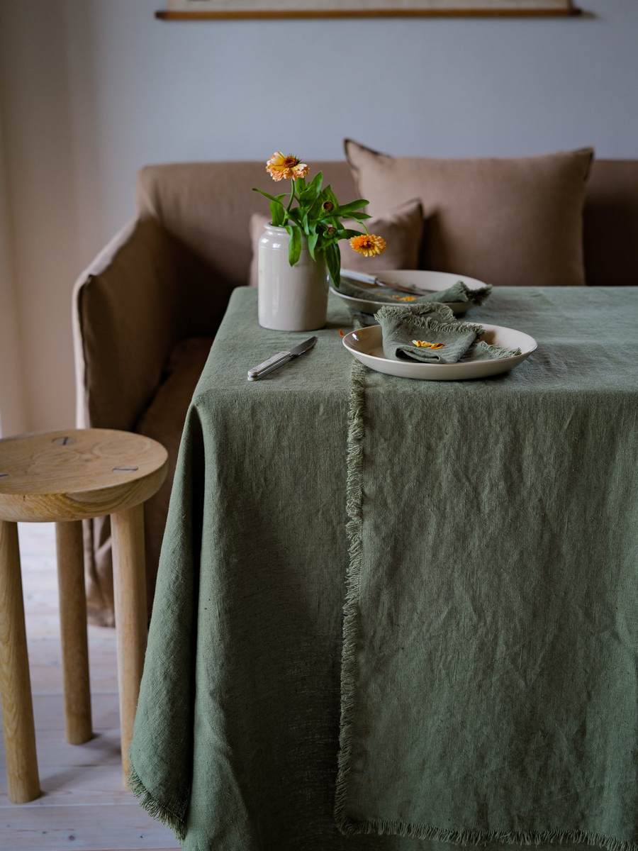 Olive green fringed linen tablecloth with cream plates and a flower vase