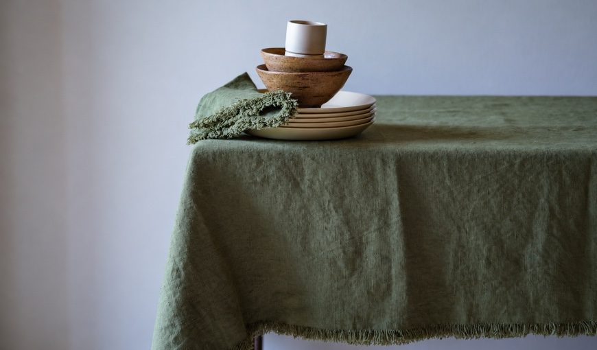 Olive green Terra Fringe linen tablecloth and napkin with cream plates and wooden bowls