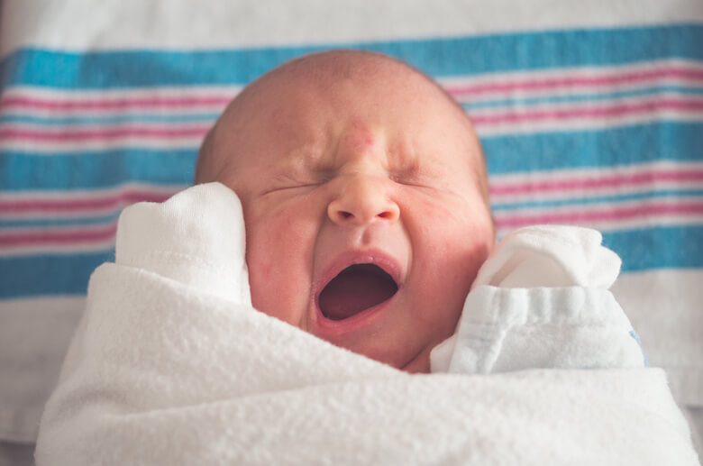 Newborn baby yawning in a white blanket